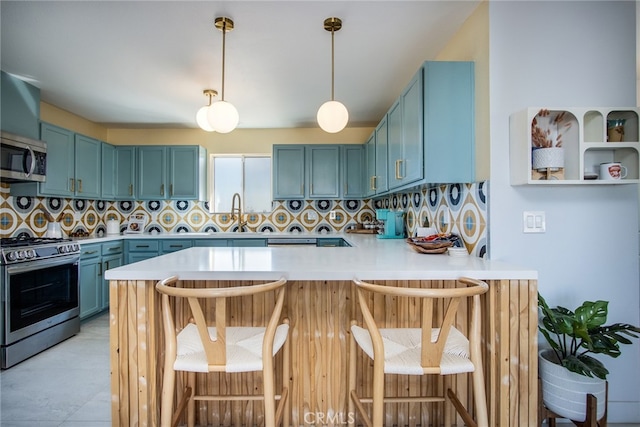 kitchen featuring blue cabinets, kitchen peninsula, backsplash, appliances with stainless steel finishes, and a kitchen breakfast bar