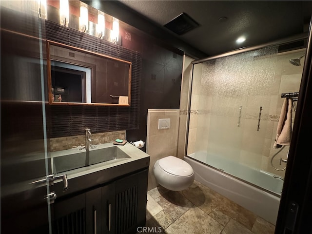 full bathroom with vanity, tile walls, toilet, and combined bath / shower with glass door