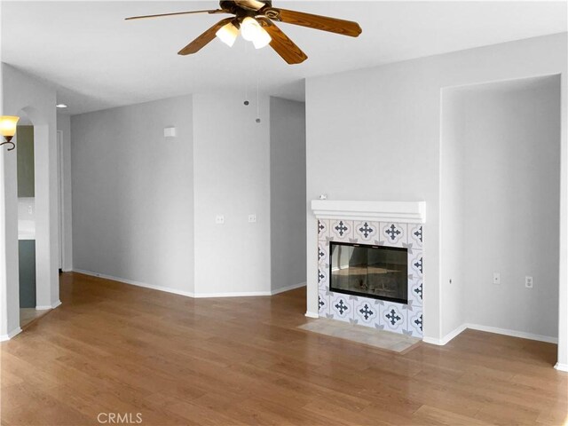 unfurnished living room with a tiled fireplace, hardwood / wood-style flooring, and ceiling fan