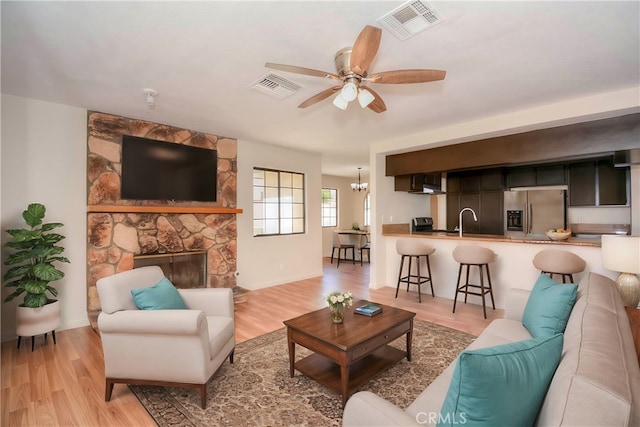 living room featuring ceiling fan with notable chandelier, sink, light hardwood / wood-style flooring, and a fireplace