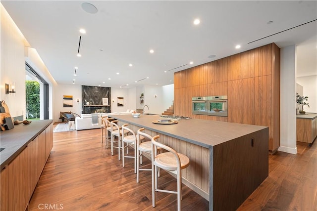 kitchen featuring oven, a spacious island, sink, light wood-type flooring, and a kitchen bar