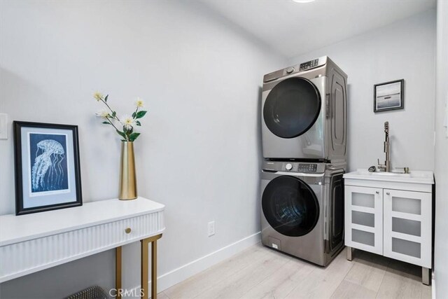 laundry room featuring cabinets, stacked washer and clothes dryer, sink, and light wood-type flooring