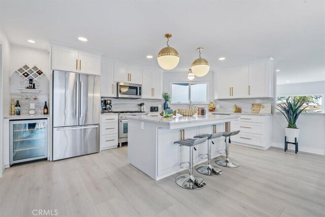 kitchen featuring appliances with stainless steel finishes, pendant lighting, white cabinets, beverage cooler, and light wood-type flooring