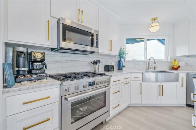 kitchen with sink, white cabinetry, stainless steel appliances, light stone countertops, and decorative backsplash