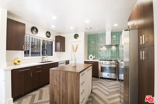 kitchen featuring tasteful backsplash, stainless steel appliances, wall chimney range hood, sink, and a center island