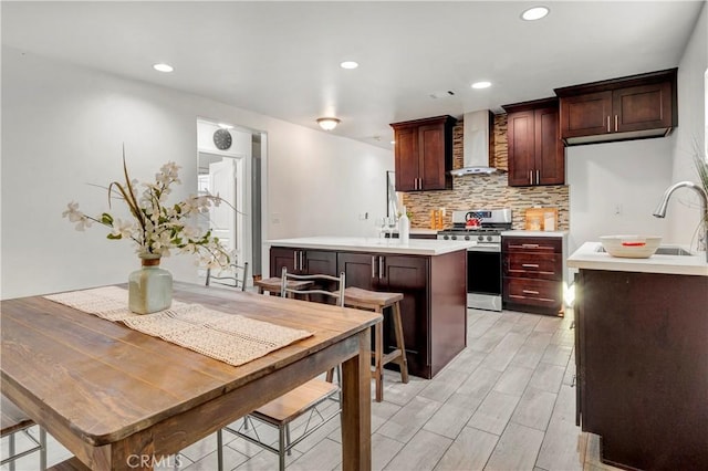 kitchen with wall chimney range hood, a kitchen island, decorative backsplash, stainless steel range with gas cooktop, and a breakfast bar area