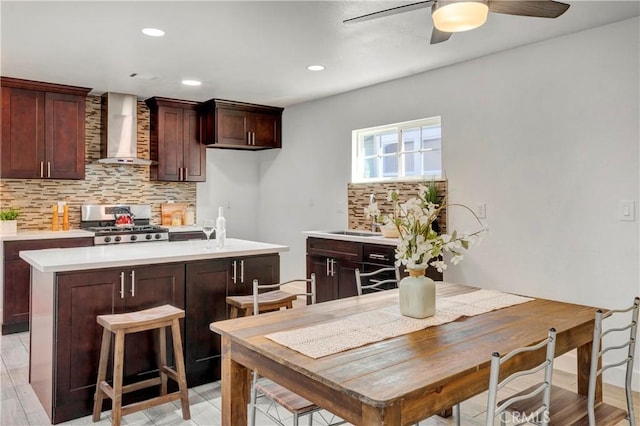 kitchen with wall chimney range hood, a kitchen island, decorative backsplash, sink, and range