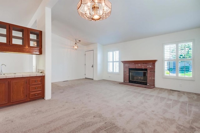 unfurnished living room with light colored carpet, a healthy amount of sunlight, a fireplace, and sink