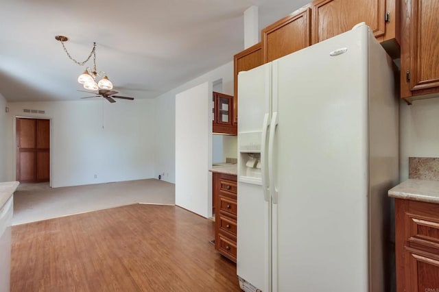 kitchen featuring light wood-type flooring, ceiling fan with notable chandelier, white fridge with ice dispenser, and decorative light fixtures