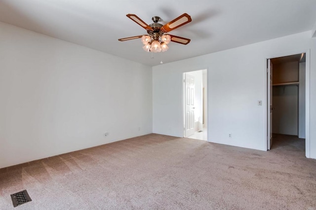 unfurnished bedroom with a spacious closet, a closet, light carpet, and ceiling fan