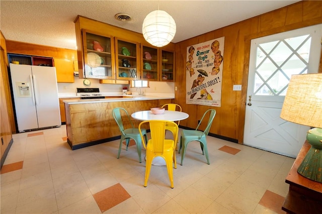 kitchen with kitchen peninsula, decorative light fixtures, black range, white fridge with ice dispenser, and wood walls