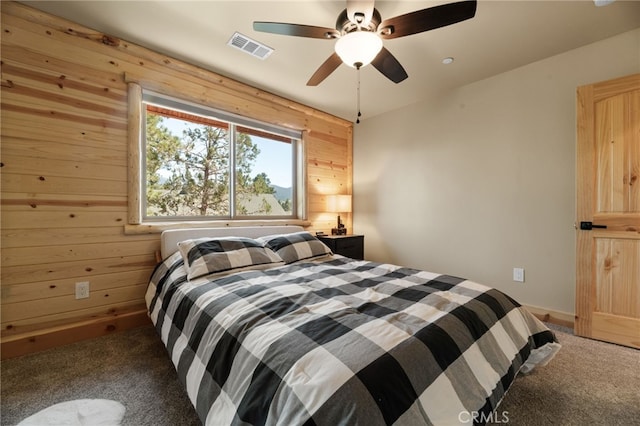 carpeted bedroom with ceiling fan and wood walls