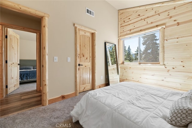 carpeted bedroom featuring visible vents, baseboards, and wooden walls