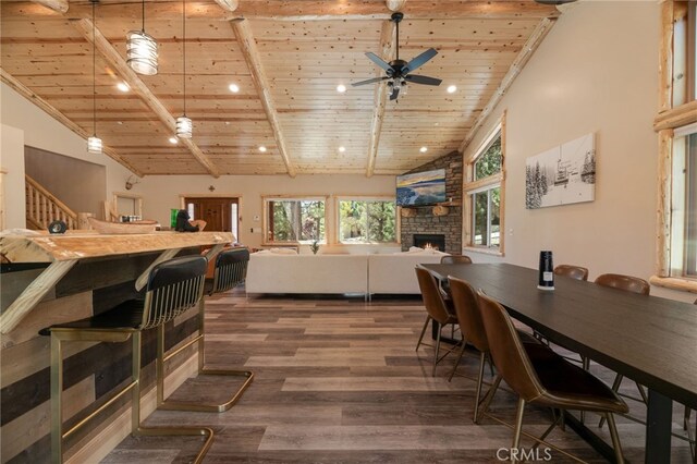 dining room featuring beamed ceiling, ceiling fan, a stone fireplace, dark hardwood / wood-style floors, and wooden ceiling