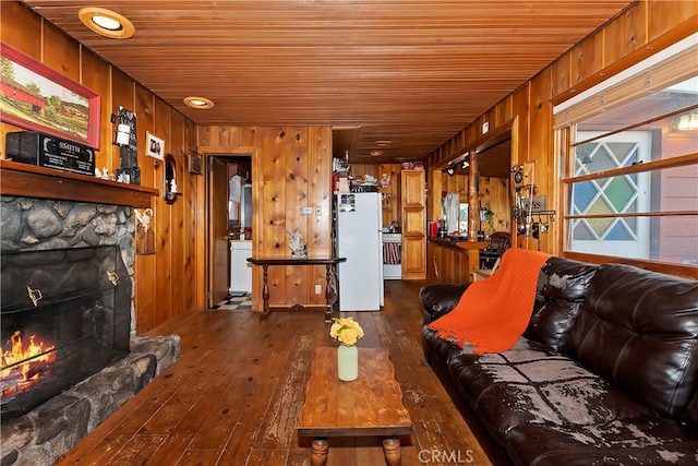 living room featuring dark wood-type flooring, wood walls, a stone fireplace, and wood ceiling