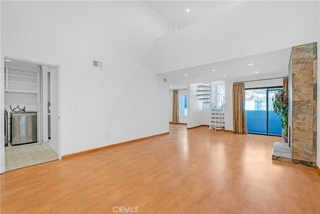 unfurnished living room featuring light hardwood / wood-style floors, washer / dryer, and a high ceiling