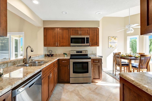 kitchen featuring light stone countertops, ceiling fan, sink, stainless steel appliances, and light tile patterned floors