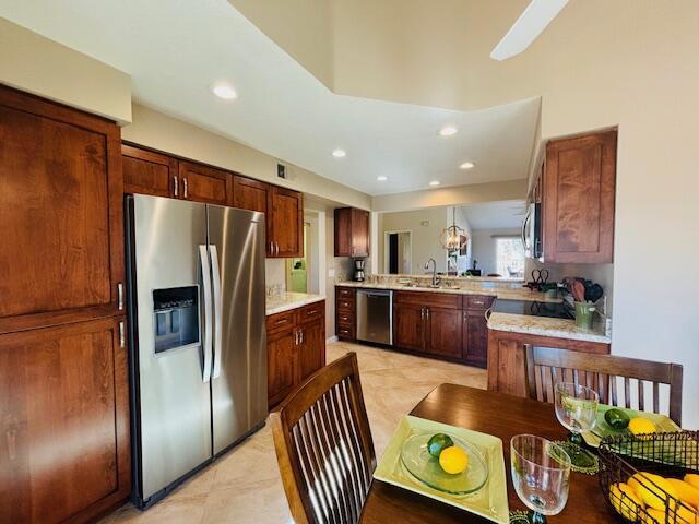 kitchen with kitchen peninsula, appliances with stainless steel finishes, sink, light tile patterned floors, and decorative light fixtures