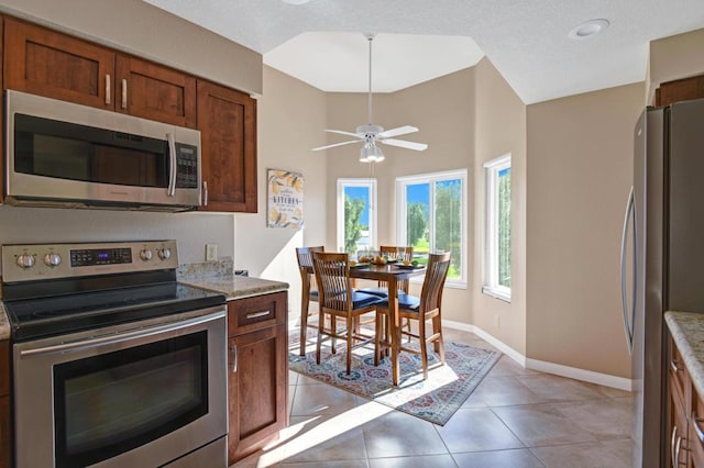 kitchen with ceiling fan, light stone countertops, a towering ceiling, light tile patterned flooring, and stainless steel appliances