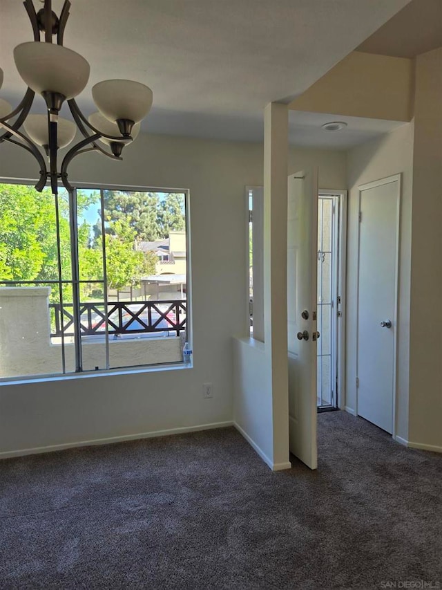 spare room with dark colored carpet and an inviting chandelier