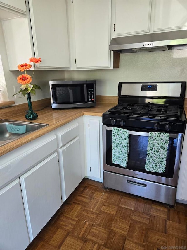 kitchen with dark parquet floors, stainless steel appliances, white cabinets, ventilation hood, and sink