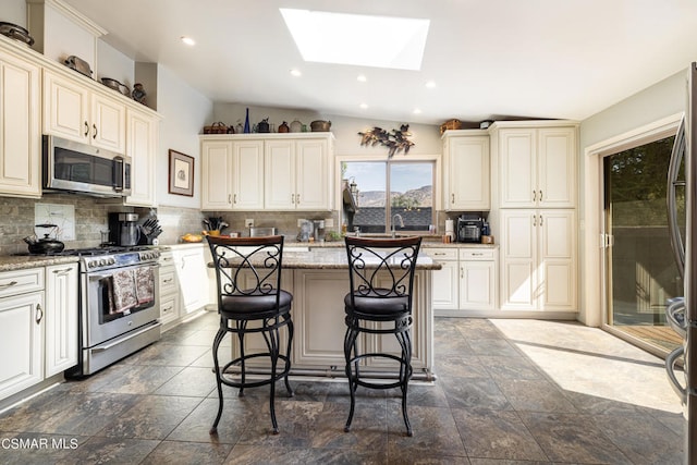 kitchen with light stone countertops, a center island, a kitchen bar, lofted ceiling with skylight, and appliances with stainless steel finishes