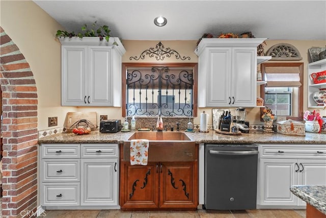 kitchen featuring light stone counters, white cabinetry, stainless steel dishwasher, and sink