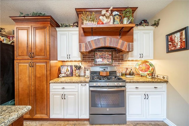 kitchen with stainless steel gas range oven, a textured ceiling, tasteful backsplash, light stone counters, and custom range hood