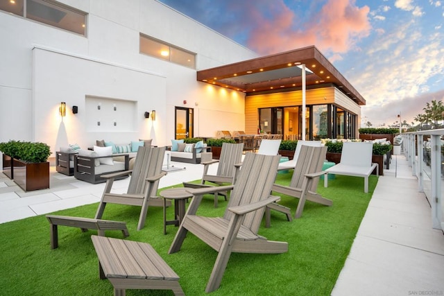 back house at dusk with an outdoor hangout area, a patio, and a lawn