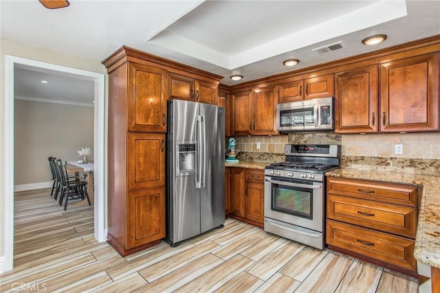 kitchen with decorative backsplash, light stone countertops, appliances with stainless steel finishes, and light hardwood / wood-style flooring