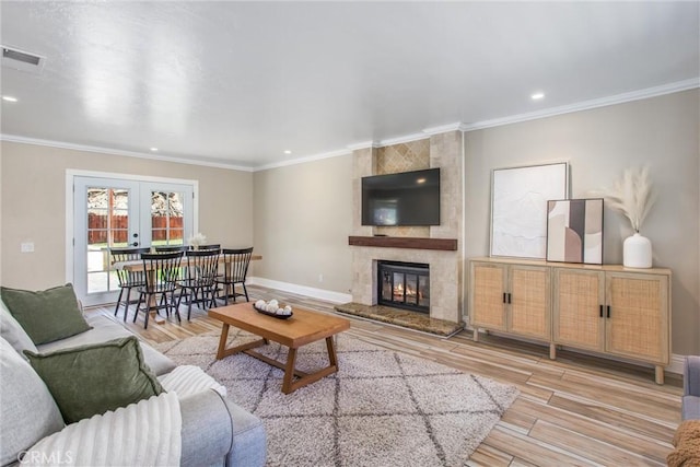 living room with french doors, light hardwood / wood-style flooring, ornamental molding, and a tiled fireplace