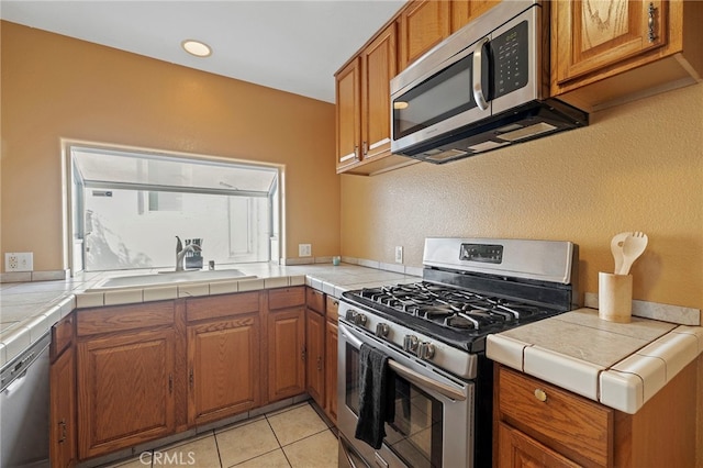 kitchen featuring appliances with stainless steel finishes, tile counters, sink, and light tile patterned floors