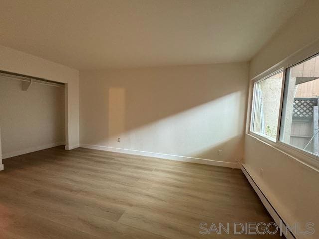 unfurnished bedroom featuring a baseboard radiator, light hardwood / wood-style flooring, and a closet