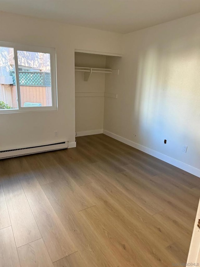 unfurnished bedroom with wood-type flooring, a closet, and baseboard heating