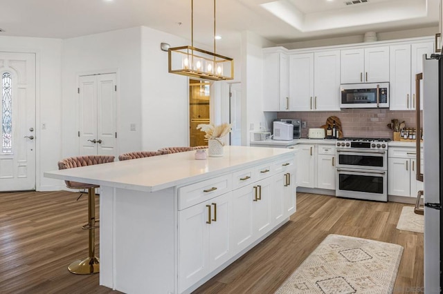 kitchen featuring a kitchen breakfast bar, light wood-type flooring, stainless steel appliances, a center island, and white cabinetry