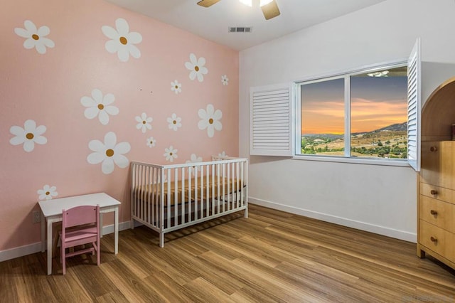 bedroom featuring hardwood / wood-style flooring, ceiling fan, and a nursery area