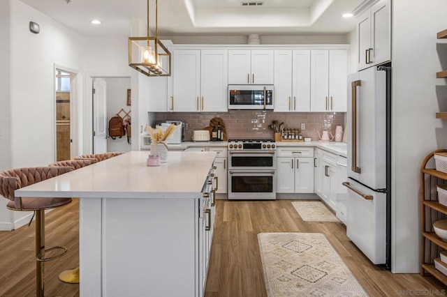 kitchen with premium appliances, pendant lighting, a breakfast bar, white cabinets, and light wood-type flooring