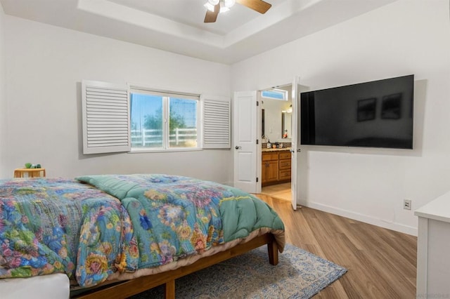 bedroom with a raised ceiling, ceiling fan, light hardwood / wood-style flooring, and ensuite bathroom