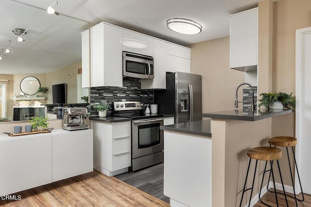 kitchen featuring kitchen peninsula, hardwood / wood-style floors, stainless steel appliances, and white cabinetry