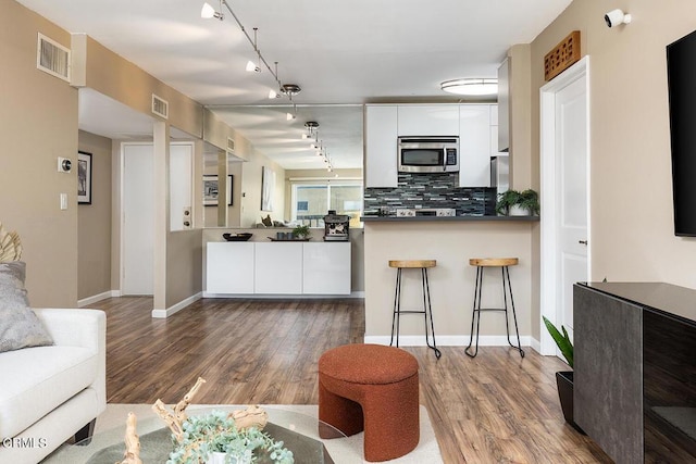 kitchen with backsplash, track lighting, hardwood / wood-style floors, white cabinetry, and a breakfast bar area