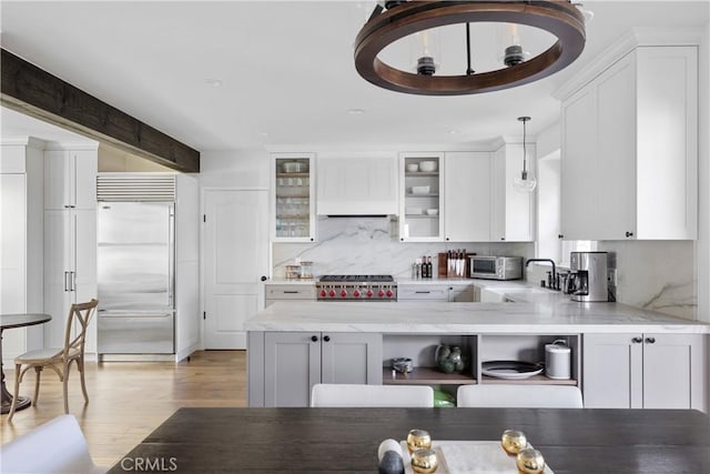 kitchen with a sink, light wood finished floors, backsplash, white cabinets, and stainless steel built in fridge