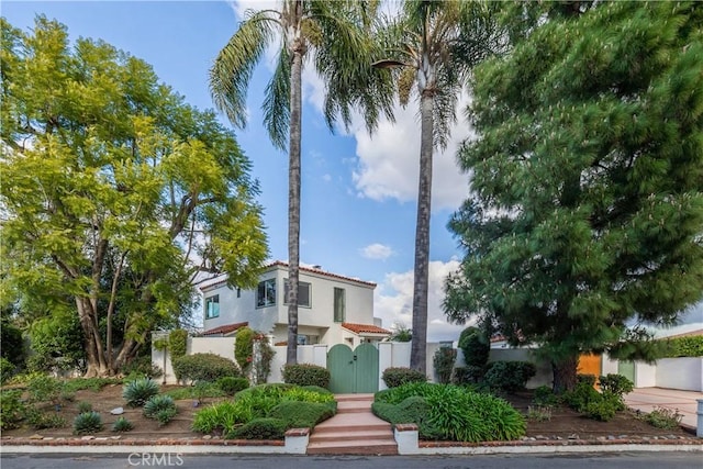 mediterranean / spanish-style home featuring a gate, a tile roof, stucco siding, and a fenced front yard