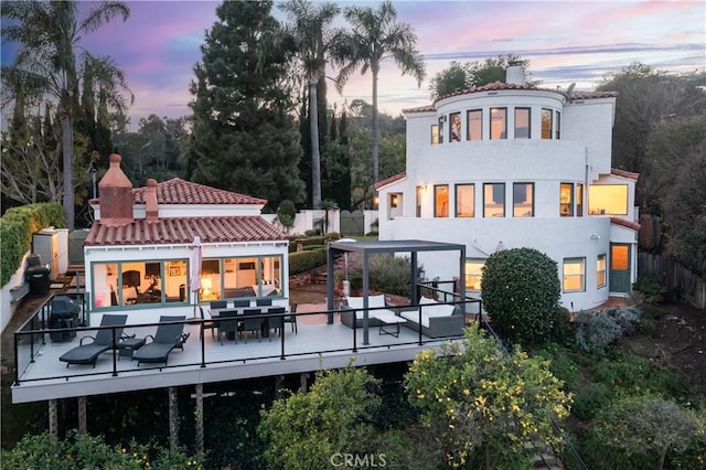 back of house at dusk with stucco siding, a wooden deck, and fence