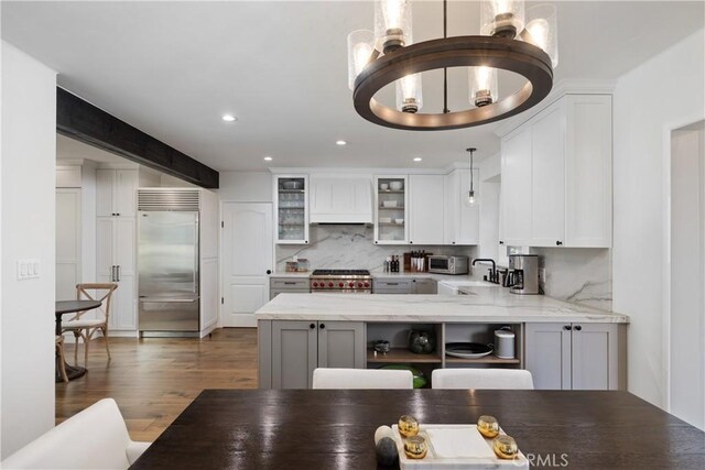 kitchen with kitchen peninsula, light stone counters, decorative light fixtures, high quality appliances, and dark hardwood / wood-style floors