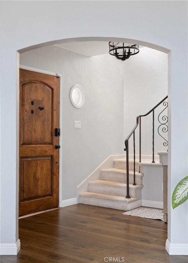 foyer entrance with arched walkways, stairs, baseboards, and wood finished floors
