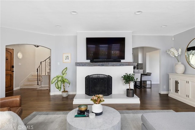 living room with wood finished floors, baseboards, arched walkways, a fireplace with raised hearth, and stairs