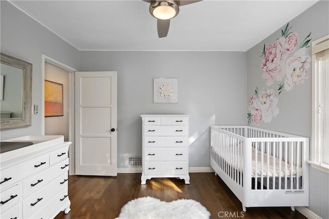 bedroom with baseboards, a nursery area, a ceiling fan, and wood finished floors