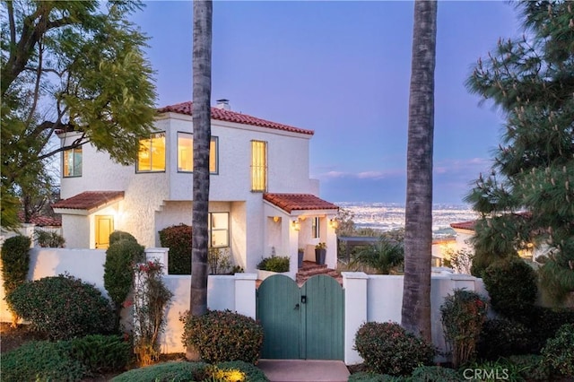 mediterranean / spanish-style house featuring a tiled roof, stucco siding, a gate, and a fenced front yard