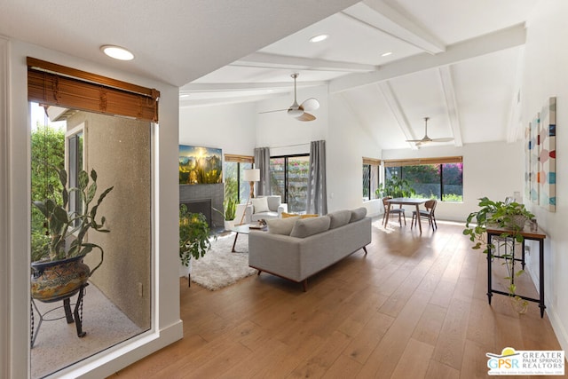 living room featuring light wood-type flooring, ceiling fan, a healthy amount of sunlight, and vaulted ceiling with beams