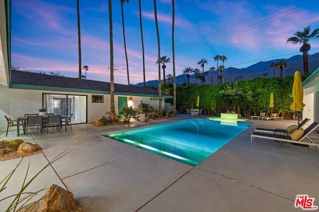 pool at dusk with a mountain view and a patio